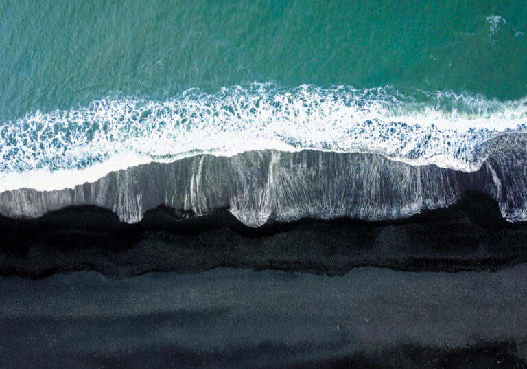 Luftaufnahme eines Strands mit schwarzem Sand
